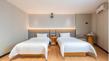 Habitación de hotel con dos camas, una mesita de noche con lámpara, una silla y un equipo de aire acondicionado.