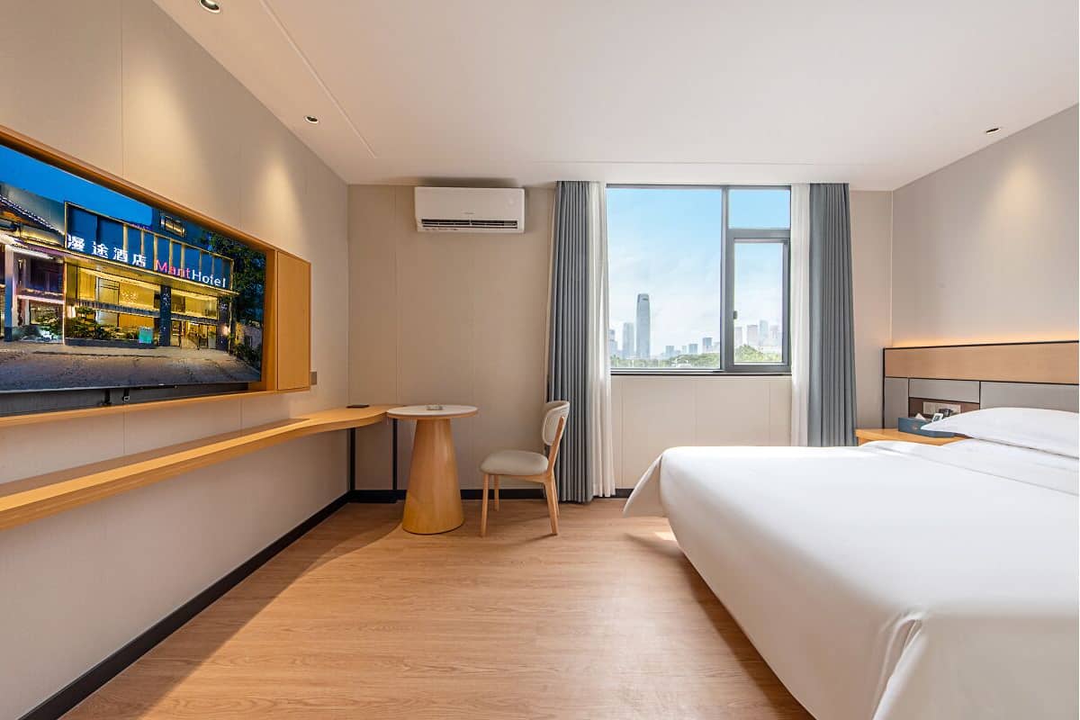 Une chambre d’hôtel équipée d’un lit, d’un bureau, d’une chaise, d’une fenêtre donnant sur la ville et d’un appareil de climatisation.