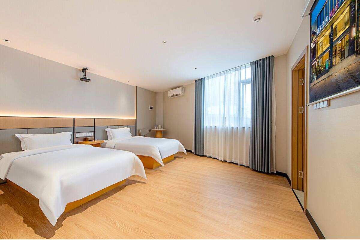Une chambre d’hôtel avec deux lits, un plancher en bois, une grande fenêtre avec des rideaux et un climatiseur fixé au mur.