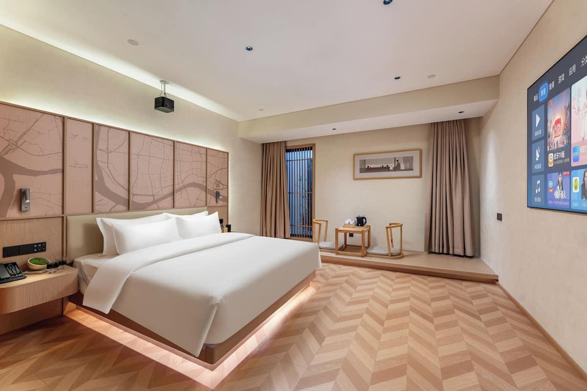 Ein modernes Hotelzimmer mit einem großen Bett, einem Schreibtisch mit Telefon, einem kleinen Tisch mit einer Tasse, einer Karte an der Wand und einem Fernsehbildschirm, der eine Speisekarte zeigt.