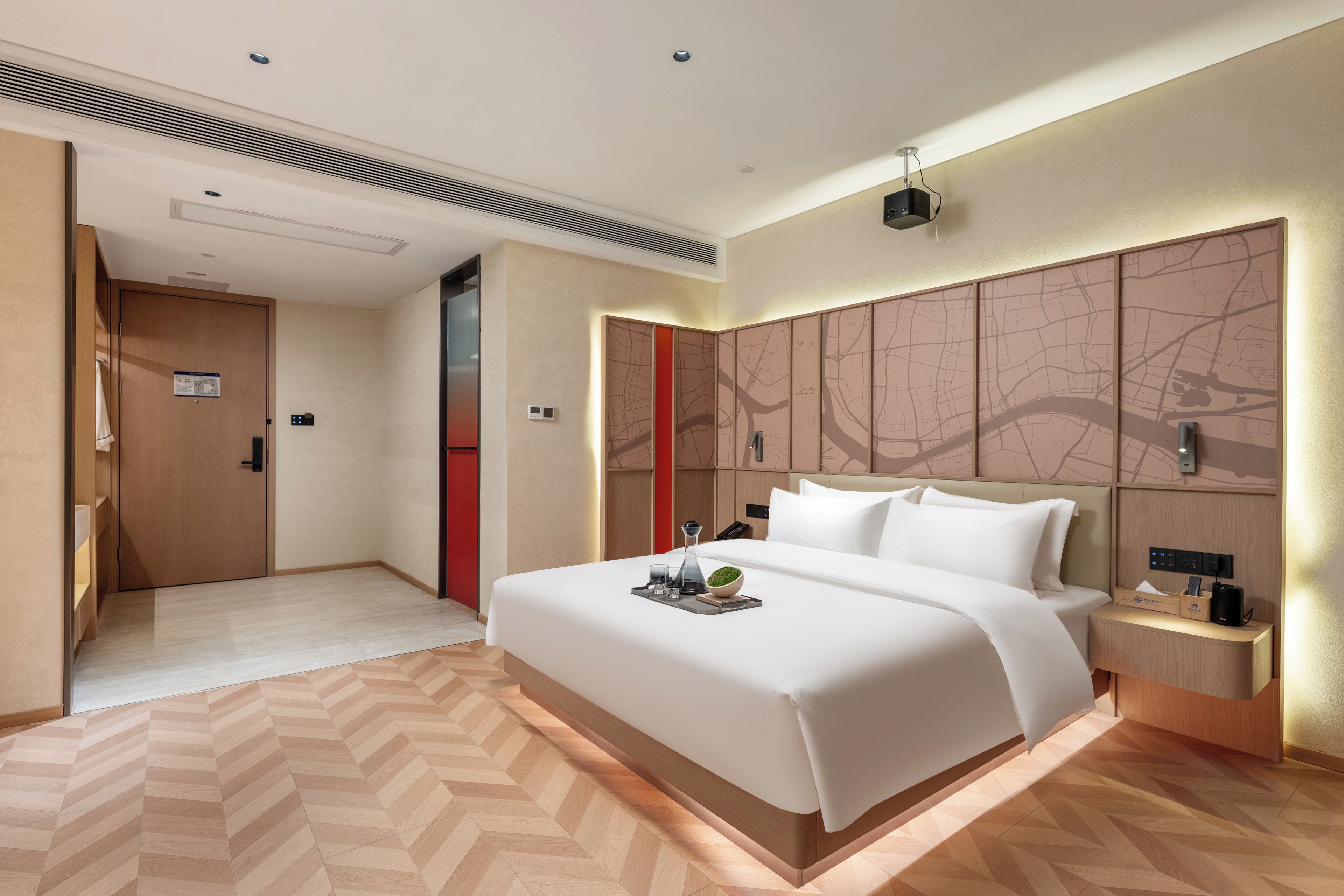 A modern hotel room with a large bed, a bedside table with a lamp, and a wall-mounted TV.