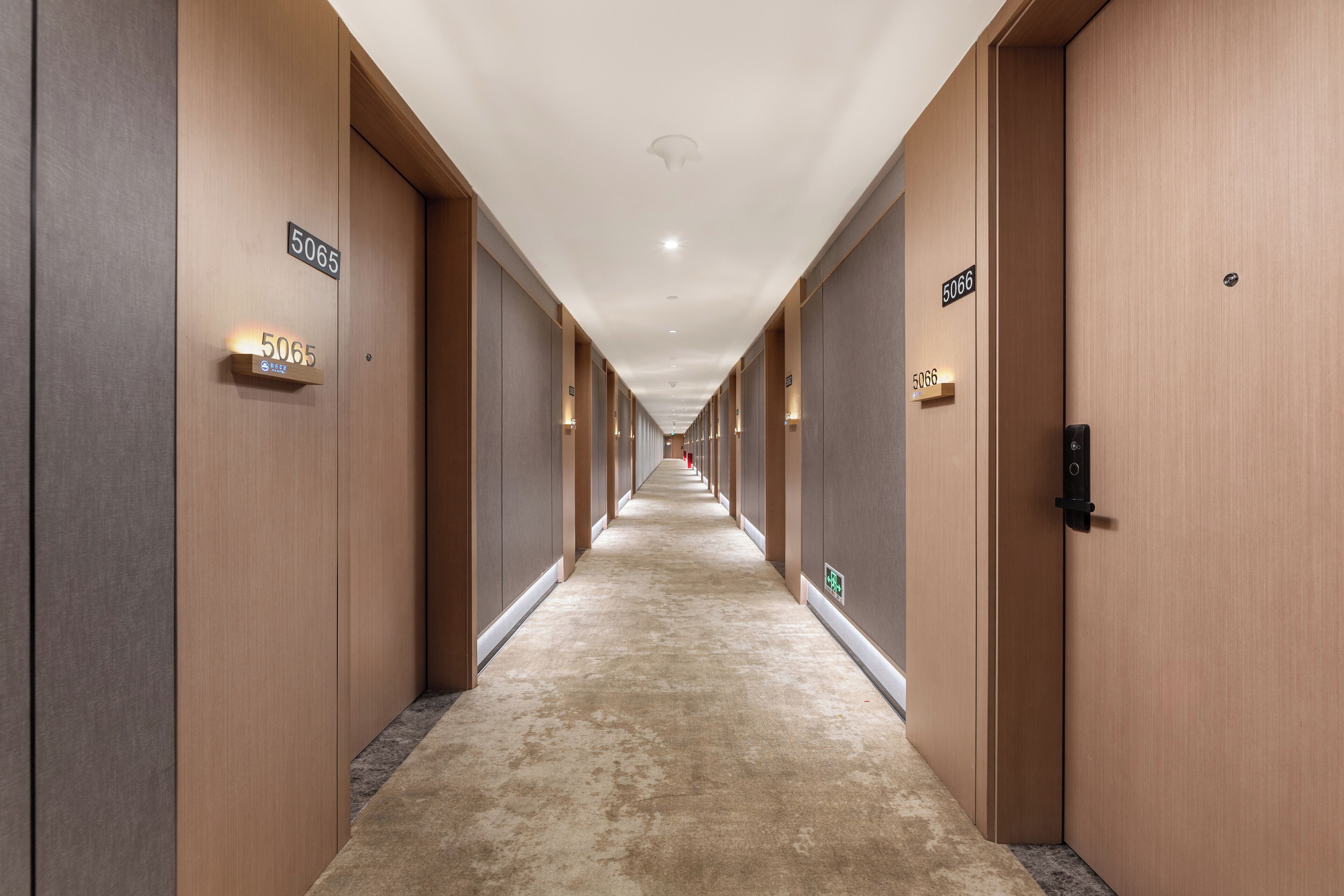 A long, narrow hallway with doors labeled 5065 and 5066, featuring a carpeted floor and wooden walls.
