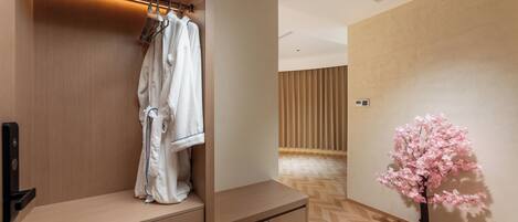 A hotel room with a wooden wardrobe, a hanging robe, a small table, and a decorative tree.