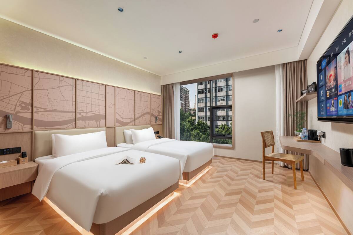 Ein modernes Hotelzimmer mit zwei Betten, einem Schreibtisch und einem Fernseher.