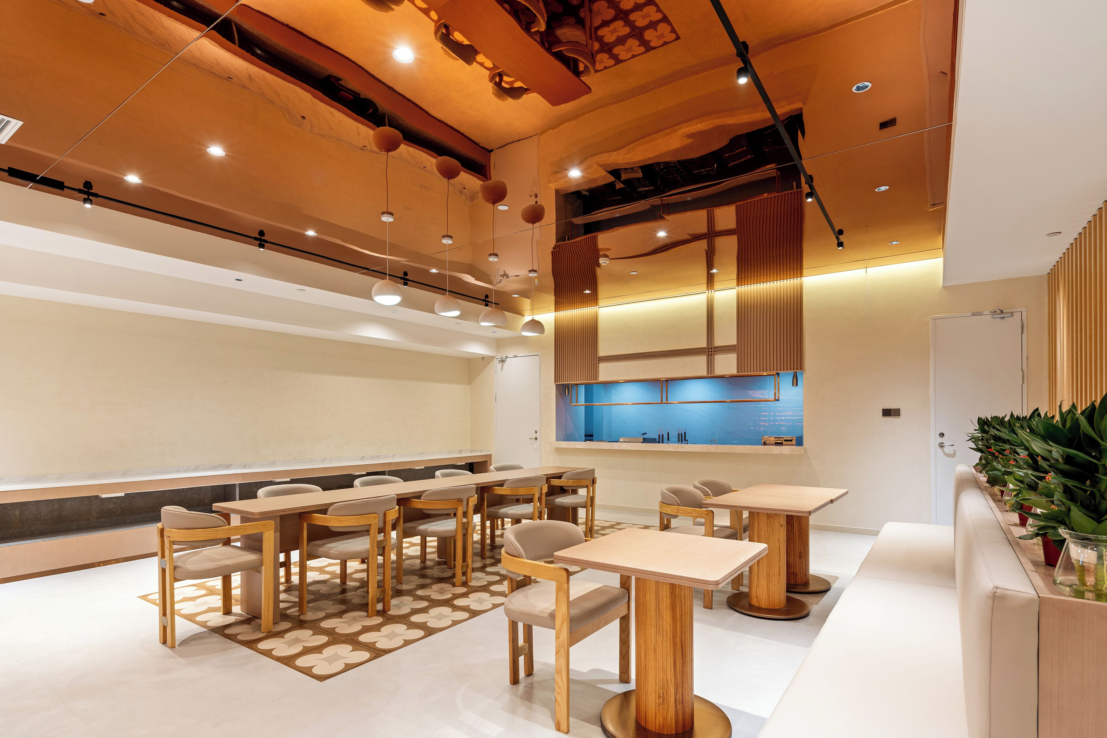 A modern dining area with wooden tables and chairs, recessed lighting, and a kitchen area in the background.