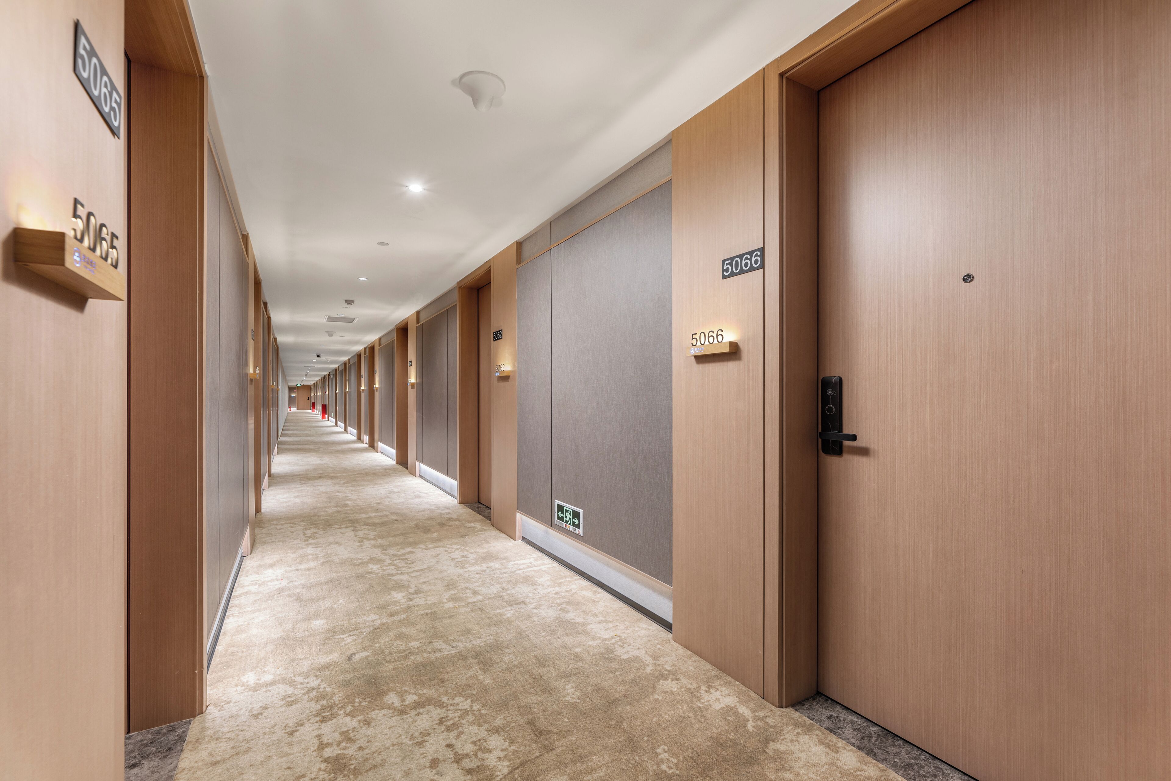 Un pasillo de hotel con puertas de madera, letreros de habitaciones numeradas y piso alfombrado.