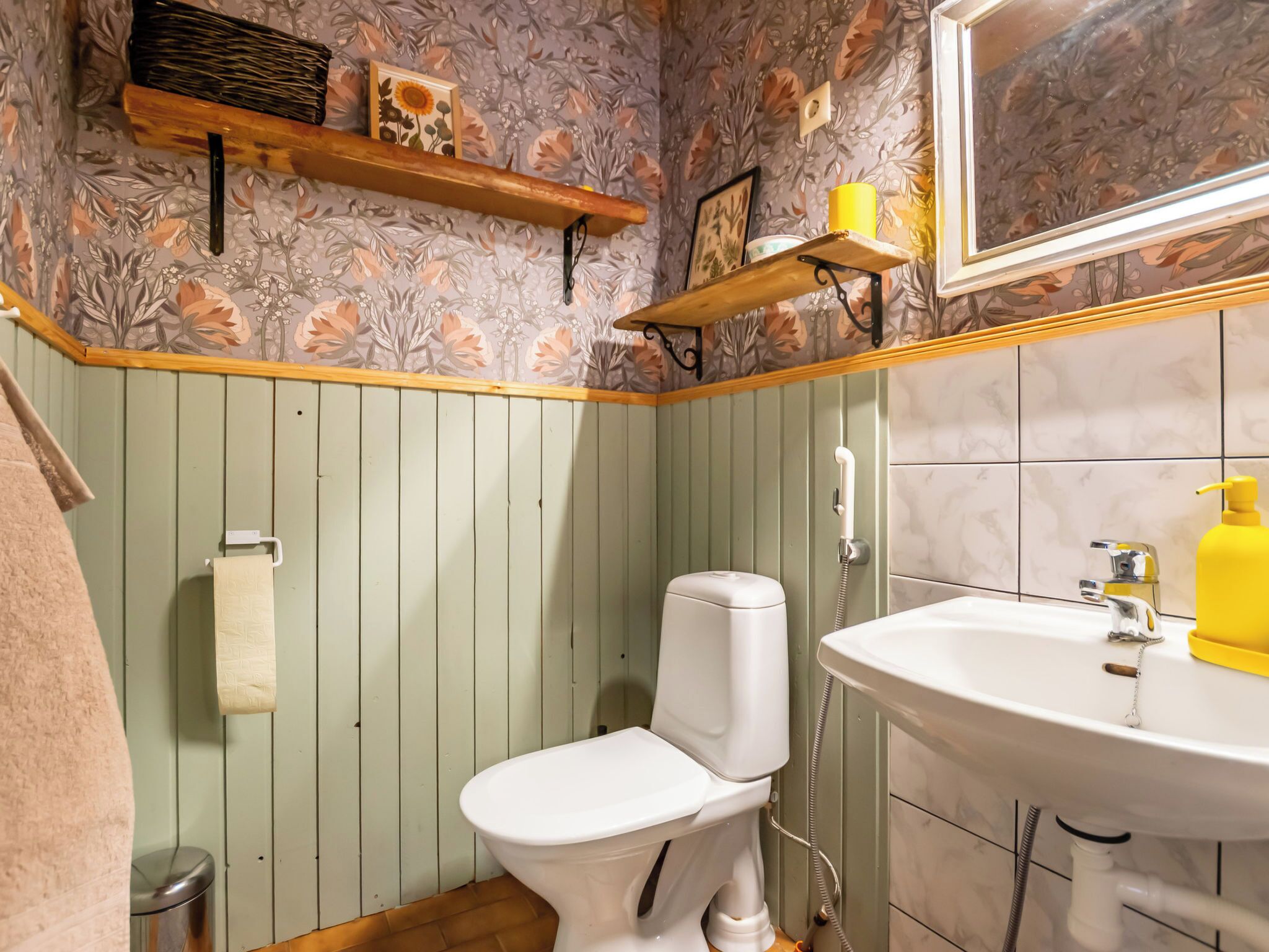 Une salle de bain comprenant des toilettes, un lavabo et une douche. On y trouve un porte-serviettes et une étagère avec des objets décoratifs.