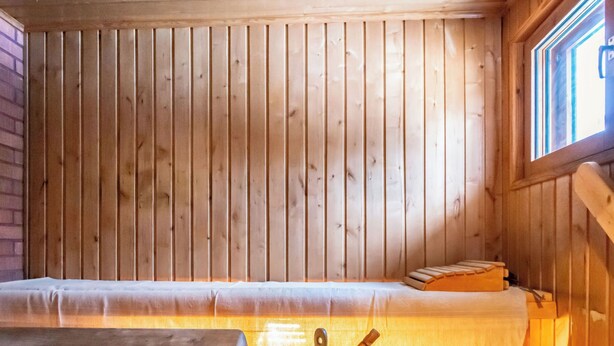 Una habitación de cabaña de madera con una cama, un banco y una olla para cocinar.