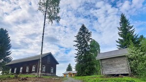 Un entorno rural con un sendero de grava que conduce a un edificio de madera con techo inclinado, rodeado de altos árboles de hoja perenne.