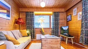 Interior acogedor de una cabaña de madera con un sofá, una mesa de centro de madera, un televisor y un adorno con forma de estrella en la ventana.