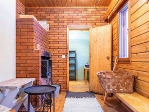 A cozy cabin interior with a brick fireplace, wooden walls, a small table, and a woven basket. - Murtolampi by Interhome (Rautalampi)