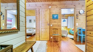 Interior de una cabaña de madera con una cama, una silla, un escritorio y un espejo.