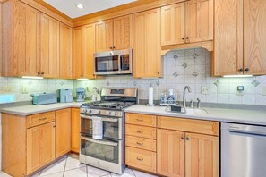 Una cocina con armarios de madera, electrodomésticos de acero inoxidable, un microondas, una estufa y un lavavajillas.