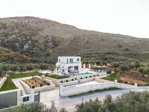 Eine moderne Villa mit Pool, umgeben von Olivenbäumen und Hügeln.