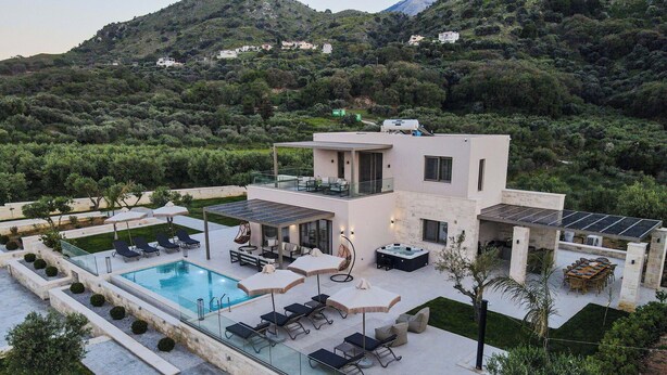 Eine moderne Villa mit Swimmingpool, Sitzgelegenheiten im Freien und Blick auf die umliegenden Hügel.