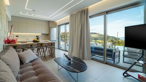 Ein modernes Wohnzimmer mit einer Couch, einem Essbereich mit Barhocker, einer Küche und einem Balkon mit Fernseher.