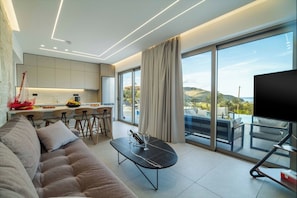 Ein modernes Wohnzimmer mit einer Couch, einem Essbereich mit Barhocker, einer Küche und einem Balkon mit Fernseher.