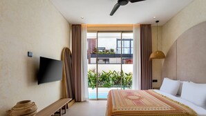 A hotel room with a bed, a bench, a television, and a view of a balcony with plants. - Villa Fresko 2 by Alfred in Bali (Munggu)