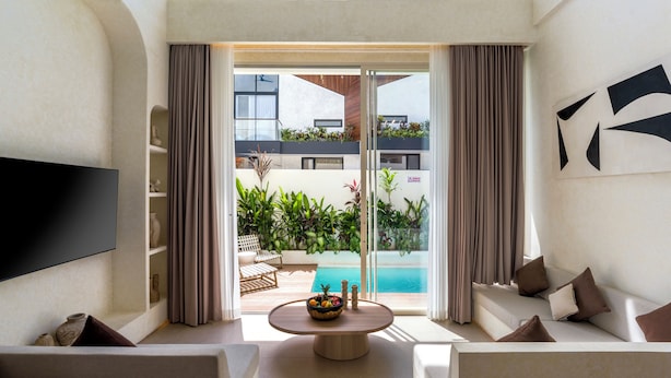 A modern living room with a flat-screen TV, a round coffee table with fruit, a sofa, and a view of a pool and outdoor area. - Villa Fresko 2 by Alfred in Bali (Munggu)