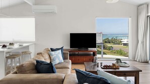 Uma sala de estar moderna com sofá, televisão, área de refeições e vista para o oceano.