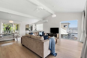 Ein großzügiger Wohnbereich mit einer Couch, einem Fernseher und einem Balkon mit Geländer.