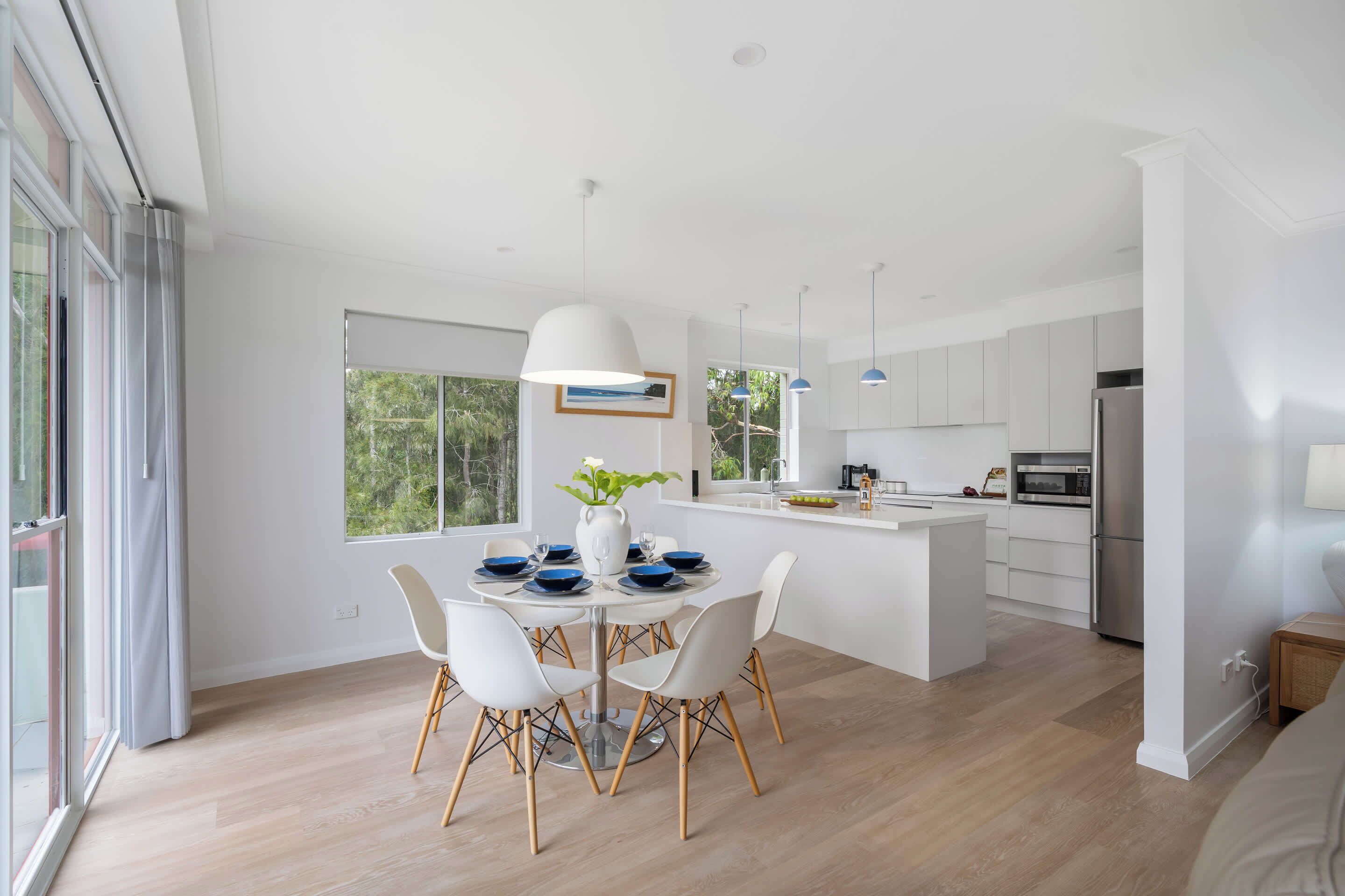 A modern kitchen with white cabinets, a central island, and a dining area with a round table and chairs.