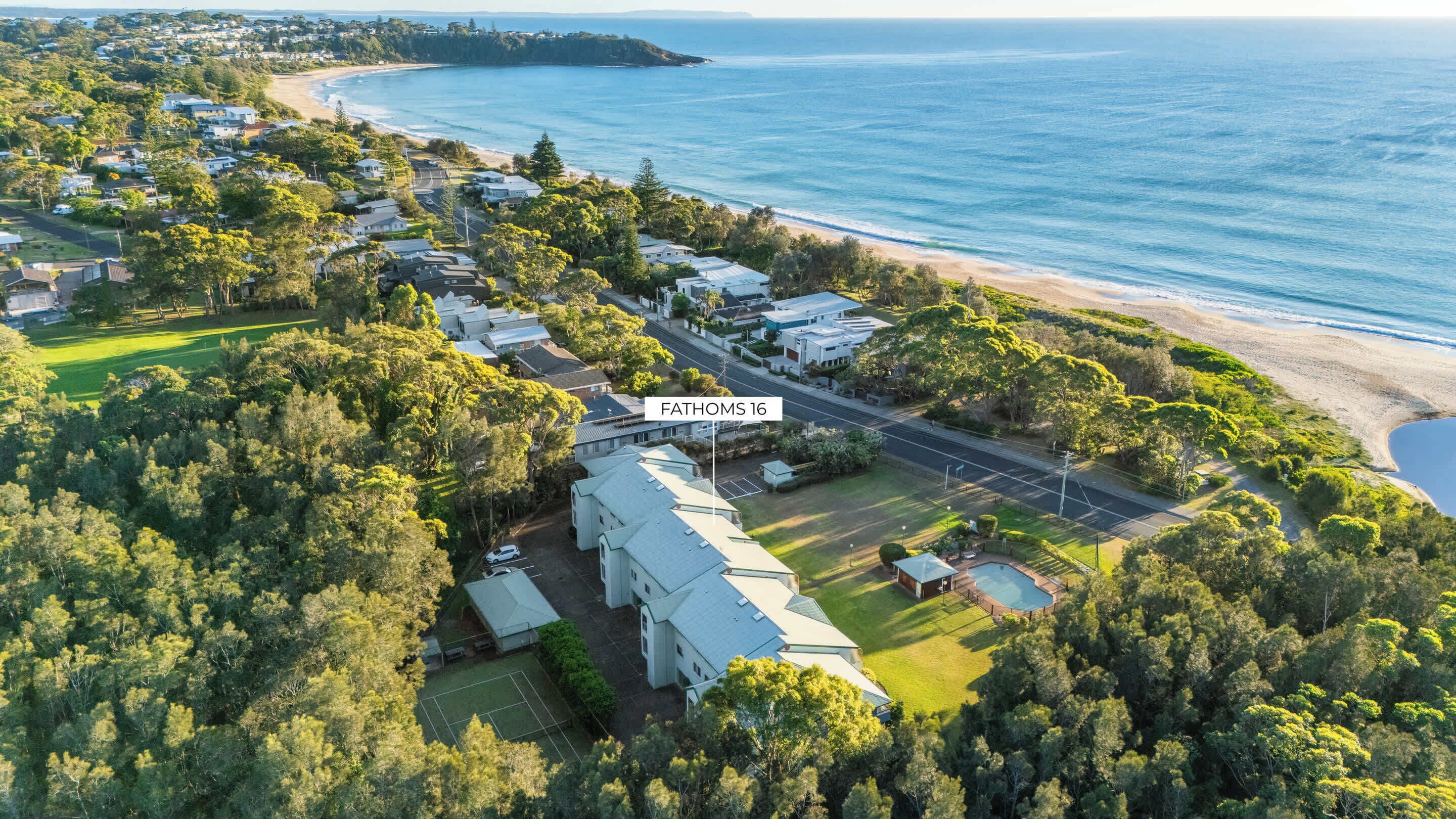 An aerial view of a coastal residential area with houses, a road, and a beach.