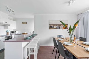 Eine moderne Küche mit weißen Schränken, einer zentralen Kochinsel mit Sitzgelegenheiten und einem Essbereich mit Holztisch und Stühlen.