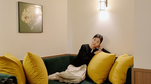 A person sitting on a green sofa with yellow pillows in a room with a framed artwork on the wall and a wall-mounted light fixture. - Stay Passport Tokyo Ryokan Seoul Sadang (Seoul)