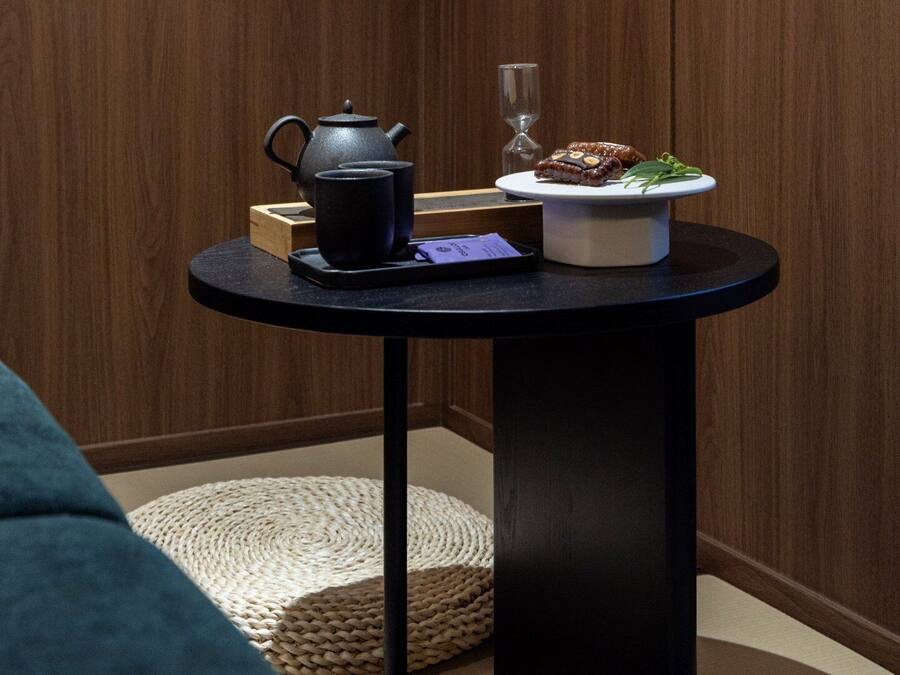 Una pequeña mesa redonda con una tetera negra, un vaso y un plato con comida.