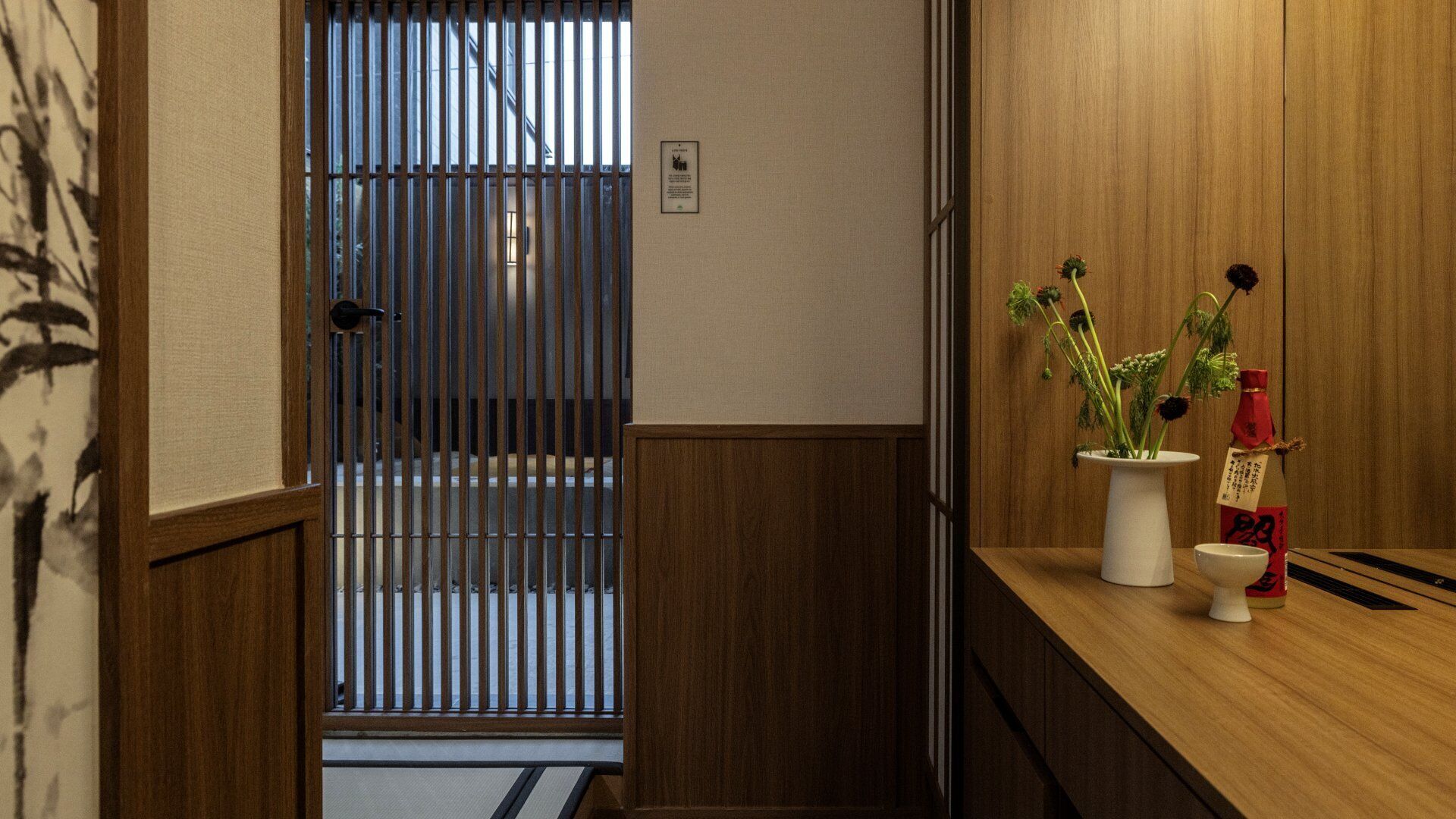 Una tradizionale stanza giapponese con porte scorrevoli, un banco reception in legno e un vaso con fiori.