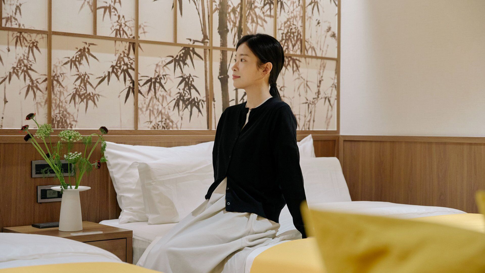 A hotel room with a bed, bedside table, and a wall with a bamboo pattern.