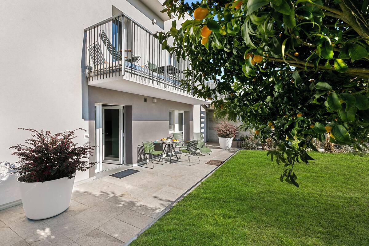 A modern building with a balcony, a patio with outdoor furniture, and a well-maintained lawn.