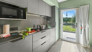 A modern kitchen with a built-in microwave, stainless steel appliances, and a view of a garden through a glass door. - Villa al Fiume (Nago-Torbole)