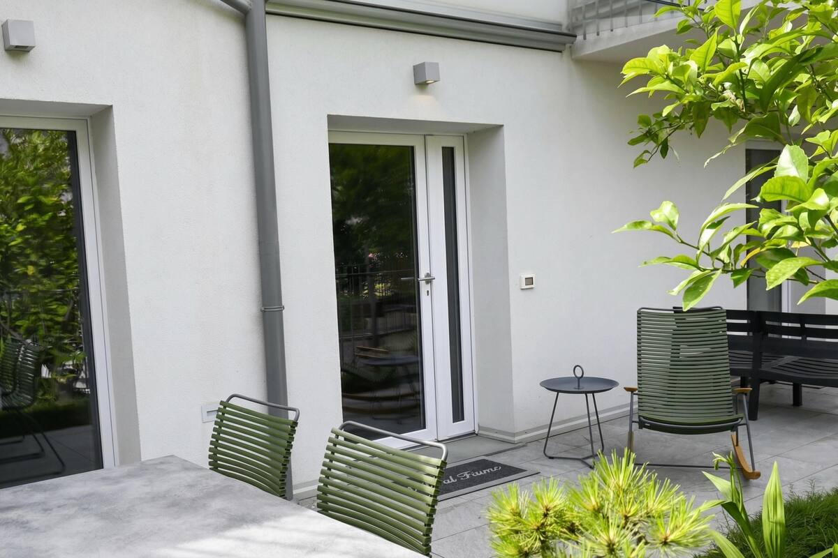 A modern outdoor patio with a glass door, a table, two chairs, and a small round table.