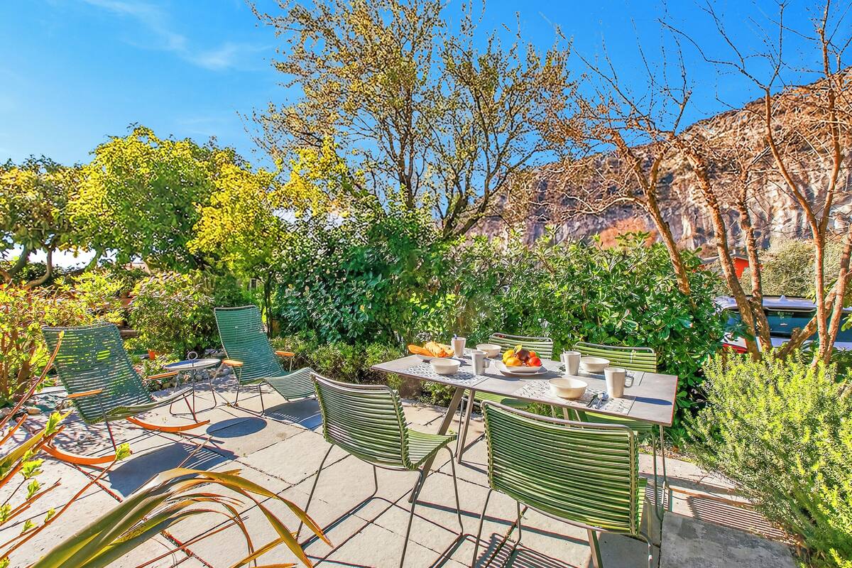 An outdoor patio with a table set for dining, surrounded by green chairs and plants.