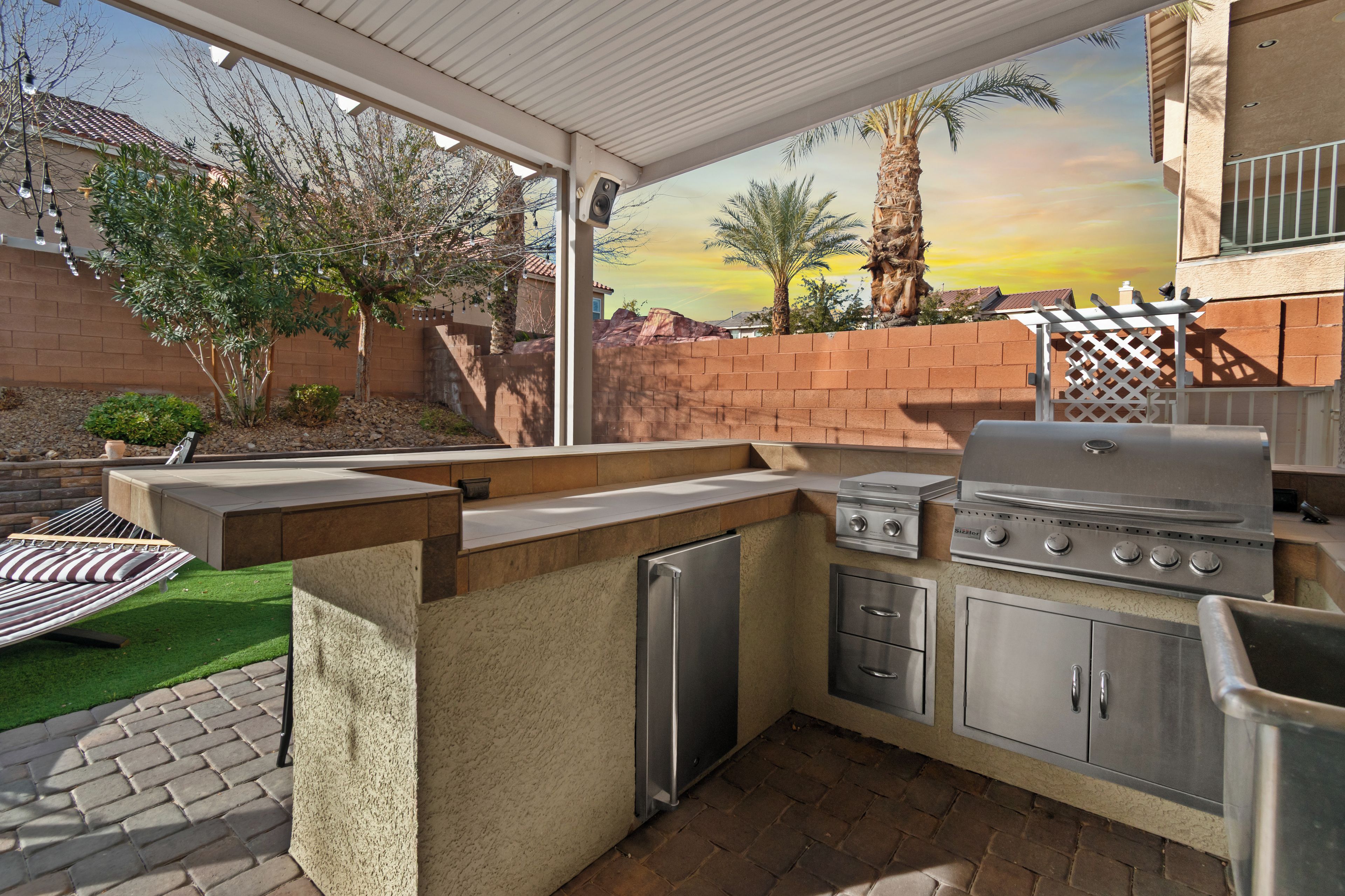 Outdoor kitchen and grill station with built-in BBQ, countertops and sink, perfect for alfresco cooking and dining. Prepare delicious meals while enjoying the resort-style backyard and desert sunsets.
