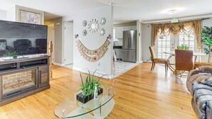 A modern living room with a glass coffee table, a fireplace, a TV, and a dining area with a table and chairs. - Remote-Work Ready: Family Home Near Pittsburgh (Monroeville)