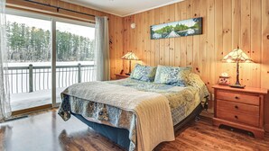 Ein Schlafzimmer mit einem großen Bett, Holzwänden, einem Deckenventilator, zwei Nachttischlampen und einem Fenster mit Blick auf Bäume und Schnee.