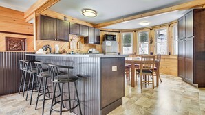 Eine Küche mit Holzausstattung, eine Bar mit Hockern, ein Esstisch mit Stühlen und ein großes Fenster.