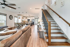 A spacious living area with a wooden staircase, a dining area, and a kitchen in the background. - Walk to Beach! 'Ocean's Paradise' w/ Patio (Mexico Beach)