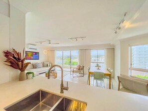 A modern living room with a kitchen area, large windows, and a dining space. - Renovated Palm Beach Ocean-View Apartment (Palm Beach)