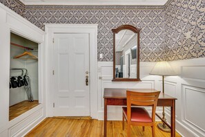 Una habitació amb un escriptori de fusta, una cadira, un mirall, una làmpada i un armari amb perruxadors.