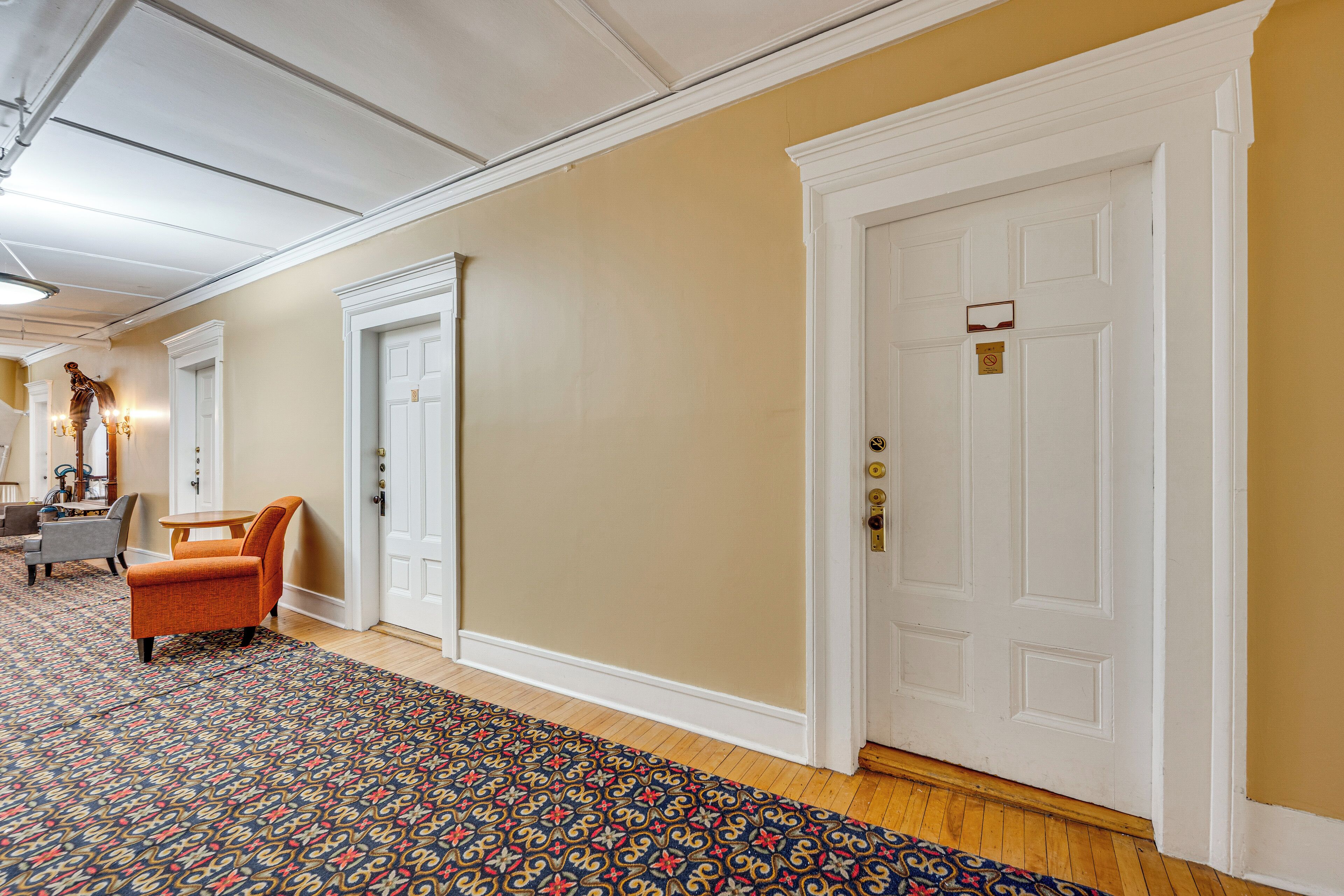 A hallway with patterned carpet, a white door, and a seating area with a chair.