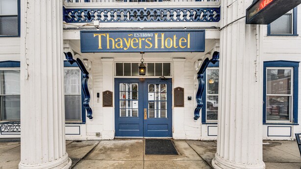 Die Fassade des Thayers Hotel mit einer blauen Eingangstür, einem Schild darüber und dekorativen Säulen.