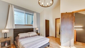Ein Schlafzimmer mit einem Bett, Nachttischen, einem Fenster mit Vorhängen, Holzboden und einer Tür.