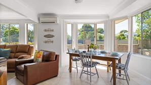 Un comedor con mesa y sillas de madera, un sofá de cuero marrón y vistas al exterior a través de amplias ventanas.