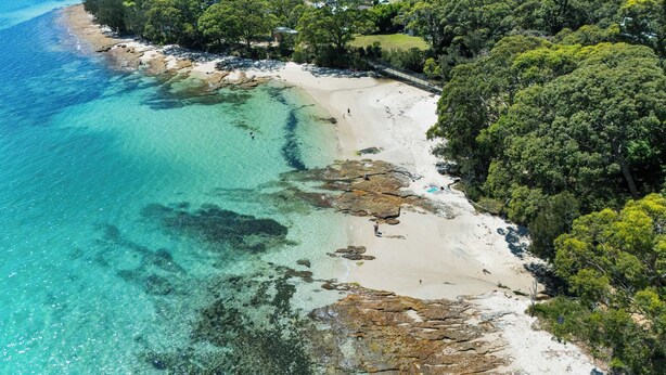 Una playa costera con aguas cristalinas, zonas rocosas y abundante vegetación.