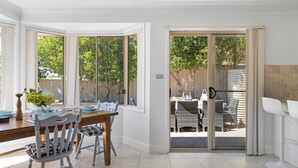 Un comedor con una mesa, sillas y vistas a un patio exterior con mobiliario de mimbre a través de una puerta corrediza de vidrio.