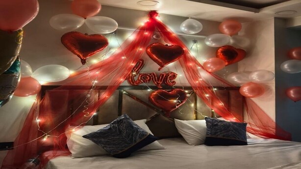 Une chambre à coucher avec un lit, des oreillers et un dais décoré de ballons et de guirlandes lumineuses en forme de cœur.